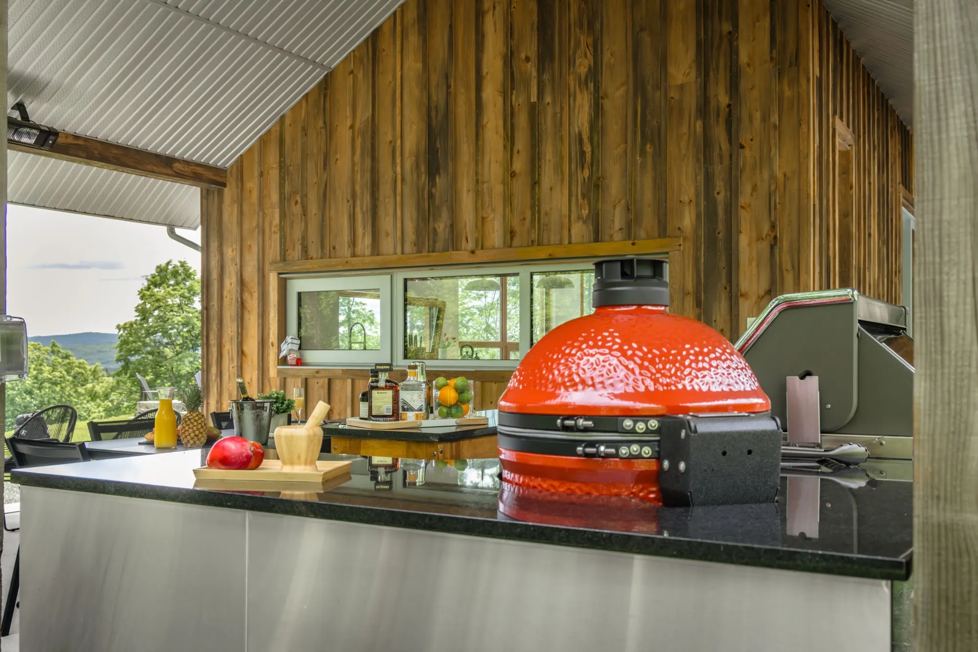 Kamado rouge sur un comptoir d'inox sous un mur de bois