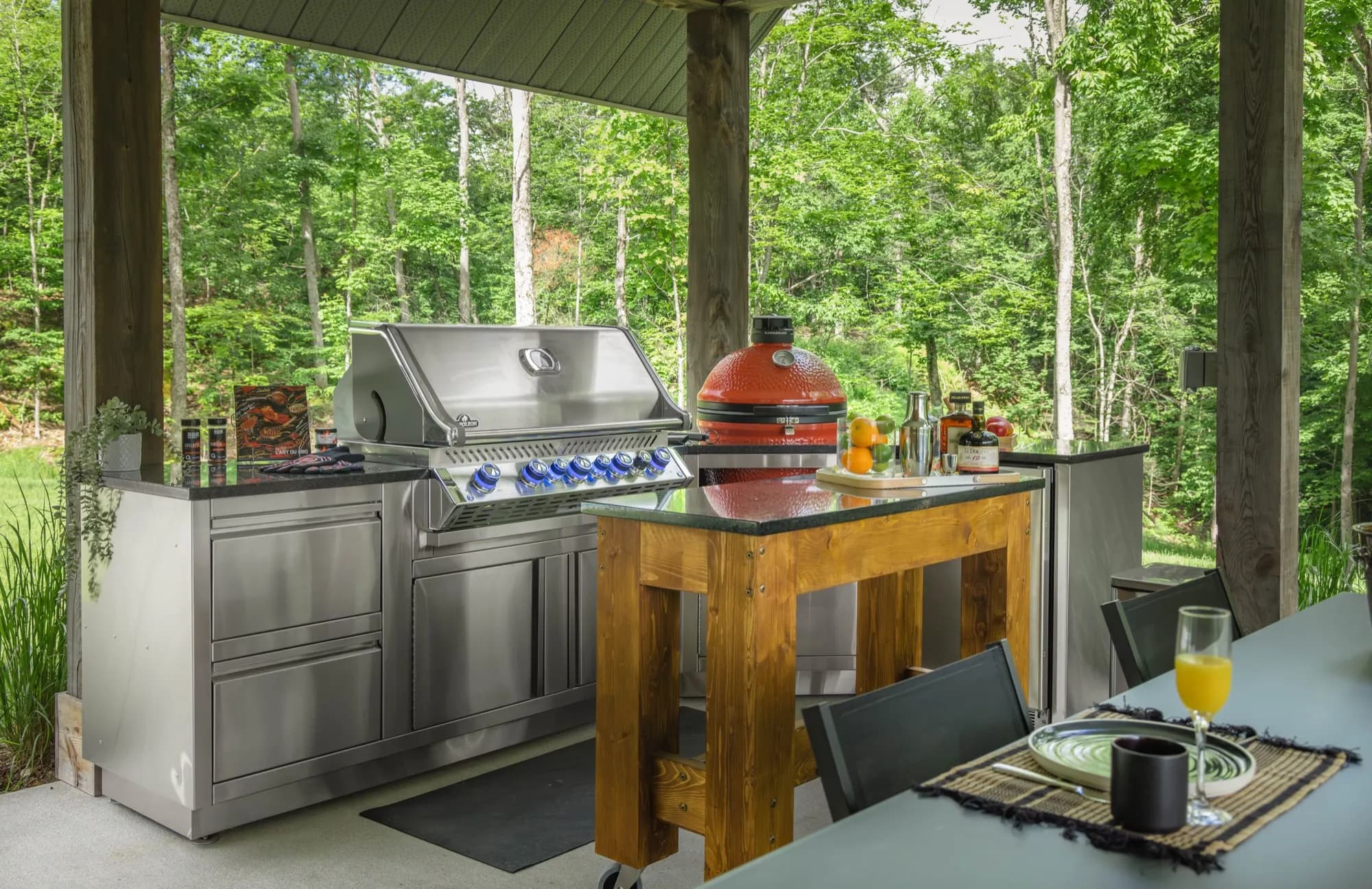 Cuisine extérieure avec gril en inox et kamado rouge sous un pavillon de bois